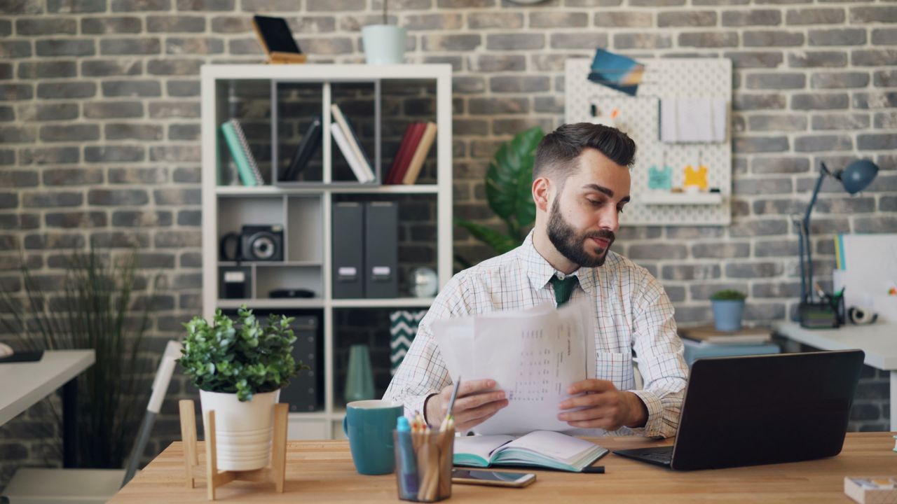 Young professional man at desk with laptop and documents in a modern office.