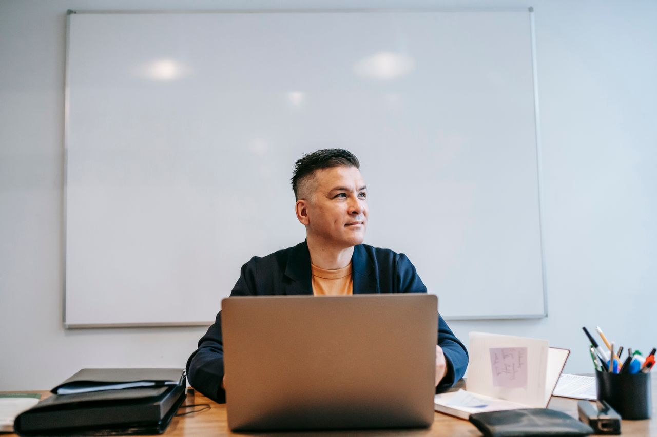 A man engaged in remote work, focused in a home office setting with a laptop and whiteboard.