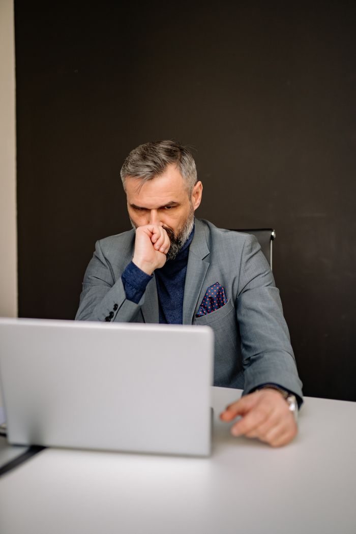 A thoughtful bearded businessman in a suit works intently on a laptop.