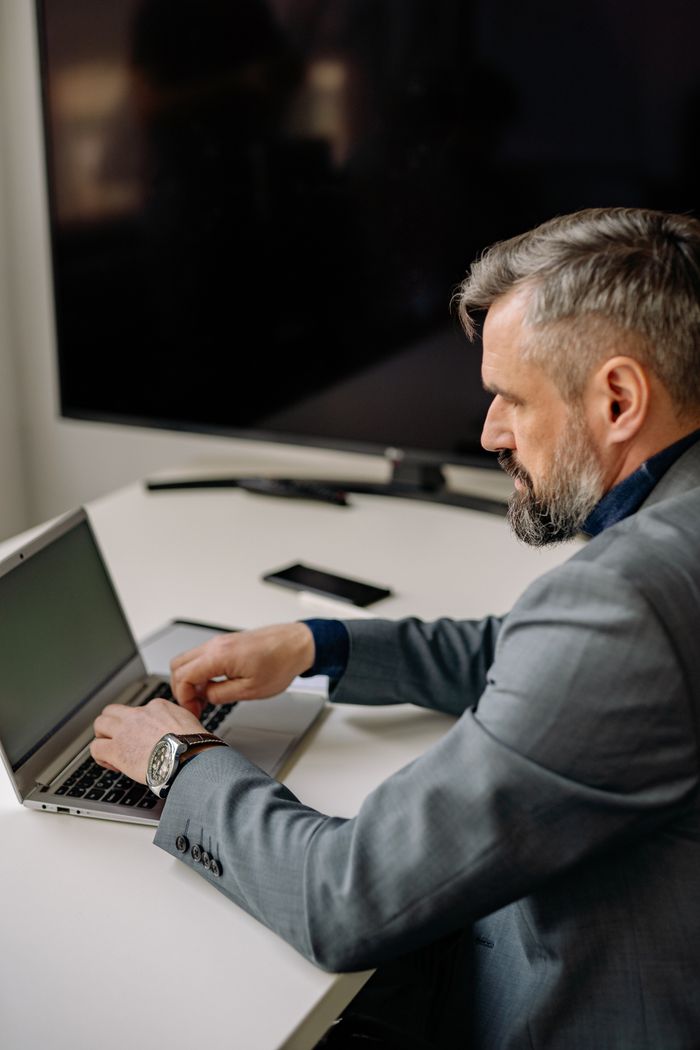 Focused adult businessman typing on a laptop at an office desk.